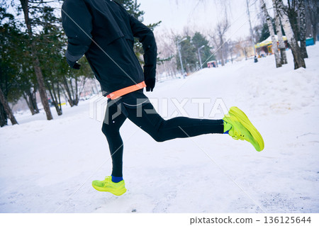 Rear view of man jogging on snowy park path in winter conditions. Rear view of man jogging on snowy park path in winter conditions. 136125644