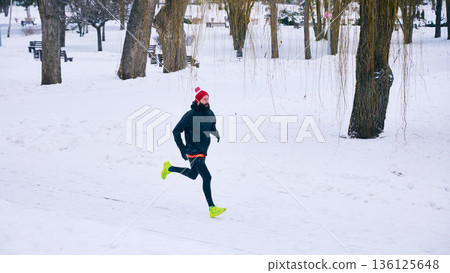 Man running in snowy park during winter workout. 136125648