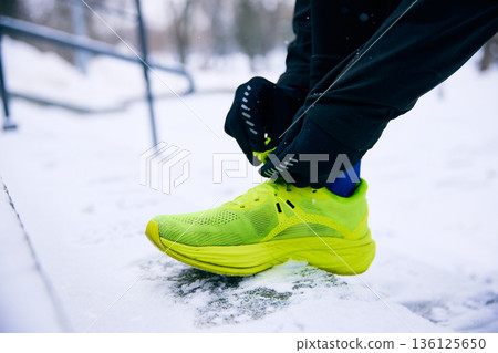 Close up of runner tying shoe laces on snowy ground. Close up of runner tying shoe laces on snowy ground. 136125650