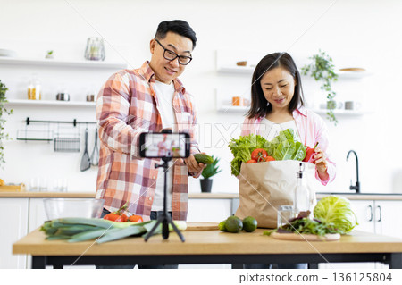 An Asian couple prepares fresh vegetables in their kitchen while recording a video blog An Asian couple prepares fresh vegetables in their kitchen while recording a video blog 136125804