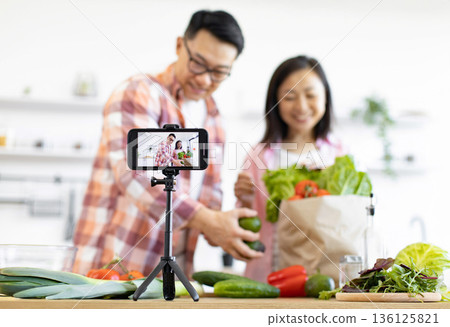 An Asian couple is filming a cooking vlog in their kitchen, surrounded by fresh produce An Asian couple is filming a cooking vlog in their kitchen, surrounded by fresh produce 136125821