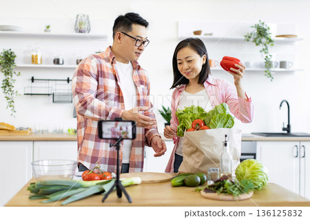 A couple prepares fresh ingredients for a cooking video in their bright kitchen A couple prepares fresh ingredients for a cooking video in their bright kitchen 136125832