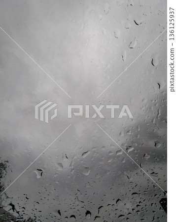 Raindrops on window pane with cloudy sky backdrop Raindrops on window pane with cloudy sky backdrop 136125937