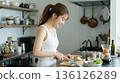 一位微笑的女士在家中明亮的廚房裡享受烹飪的樂趣。 136126289