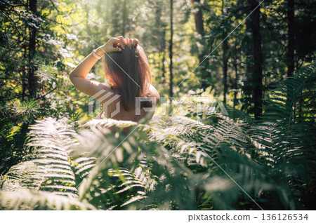 Woman in Sunlit Forest Surrounded by Ferns 136126534
