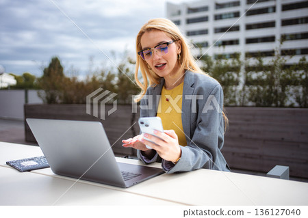 Young businesswoman multitasking outdoors with smartphone and laptop Young businesswoman multitasking outdoors with smartphone and laptop 136127040