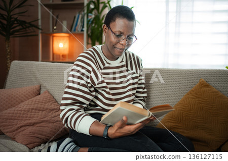 Woman enjoying reading book on couch at home Woman enjoying reading book on couch at home 136127115