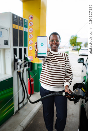 Woman refueling car showing successful mobile payment at gas station 136127122
