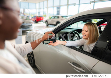 Saleswoman handing new car keys to excited customer 136127140