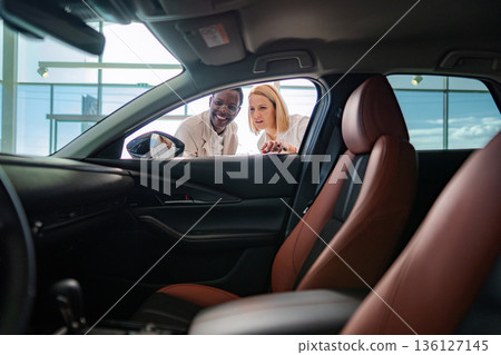 Diverse couple choosing new car at modern dealership showroom Diverse couple choosing new car at modern dealership showroom 136127145
