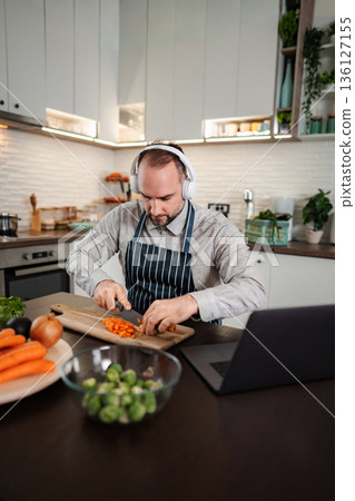 Adult man wearing headphones cooking vegetables in kitchen 136127155