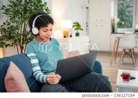 Young woman relaxing at home using laptop with headphones 136127184