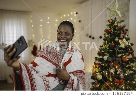 Woman taking Christmas selfie with smartphone near decorated tree Woman taking Christmas selfie with smartphone near decorated tree 136127194