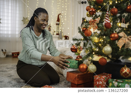 Happy woman placing Christmas gifts under festive tree 136127200