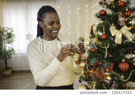Woman smiling while decorating Christmas tree for holiday season 136127202