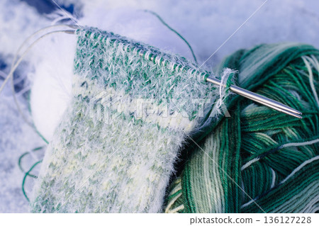 Knitted socks with knitting needles on snow. White and green gradient socks. Knitted fashion. Warm wool socks with knitting needles. Knitting hobbies. Handicraft products. Handmade knitted clothing. 136127228