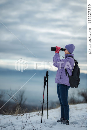 Woman hiking in winter mountains using binoculars 136127229