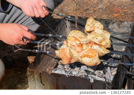 Frying meat on grill. Cook fries meat on fire. Barbecue in open air. Sunny day. Close-up. 136127285