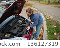 Woman checking car engine in autumn parking lot 136127319