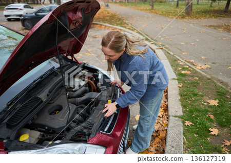 Woman checking car engine in autumn parking lot Woman checking car engine in autumn parking lot 136127319