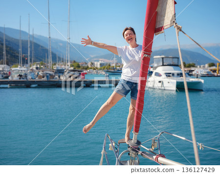 Female sailor holds white sail cloth preparing to hoist sails on yacht. Physical activity and boat handling skills are shown during preparation for sailing trip near Finike coast. Female sailor holds white sail cloth preparing to hoist sails on yacht. Physical activity and boat handling skills are shown during preparation for sailing trip near Finike coast. 136127429