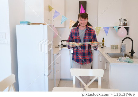 Young man celebrates his birthday at home, surrounded by a cozy and festive setting. He enjoys his special day with cake, candles, and decorations, creating memories in a warm, cheerful atmosphere. Young man celebrates his birthday at home, surrounded by a cozy and festive setting. He enjoys his special day with cake, candles, and decorations, creating memories in a warm, cheerful atmosphere. 136127469
