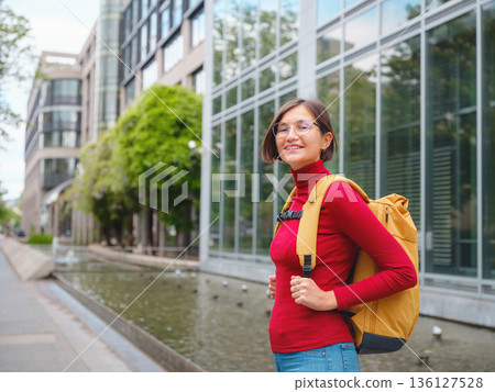 Tourist woman explores modern Frankfurt, walking through vibrant streets with contemporary architecture, skyscrapers, and urban spaces, enjoying lively atmosphere of modern side. 136127528