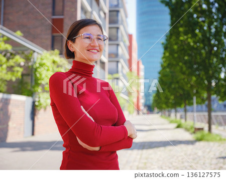 Woman in glasses and red turtleneck, dressed in business style, stands in center of Frankfurt, surrounded by modern buildings and urban life, embodying professionalism and confidence Woman in glasses and red turtleneck, dressed in business style, stands in center of Frankfurt, surrounded by modern buildings and urban life, embodying professionalism and confidence 136127575