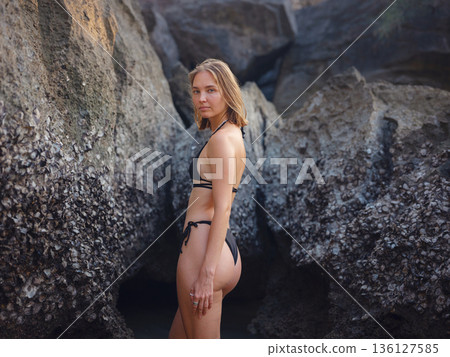Young woman enjoying serene evening at sea in Krabi, Thailand during sunset. Calm waves, golden light, and peaceful atmosphere highlight tropical beauty and connection with nature. 136127585