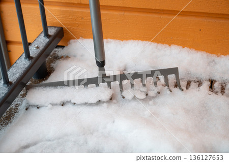 Snow removal with metal rake on wooden porch in winter home entrance 136127653