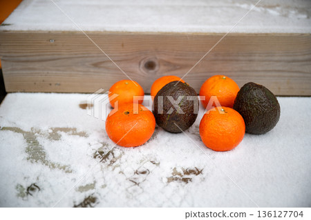 Fresh citrus fruit and avocados on snowy wooden steps in winter Fresh citrus fruit and avocados on snowy wooden steps in winter 136127704