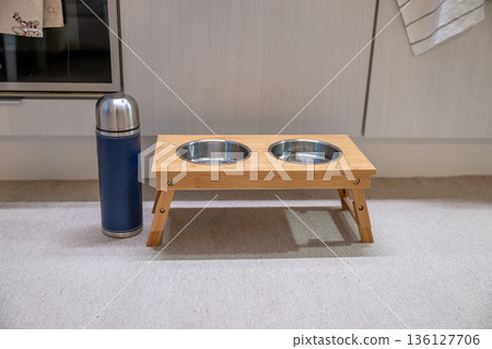 Elevated wooden pet feeding station with double bowl and thermos in modern kitchen Elevated wooden pet feeding station with double bowl and thermos in modern kitchen 136127706