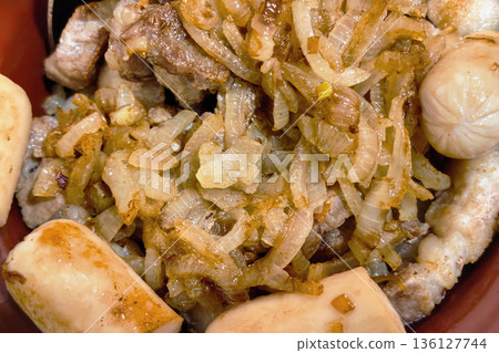 A plate shows pork pieces cooked with onions and served with boiled potatoes. The dish is placed in a bowl on a kitchen table, ready to eat 136127744