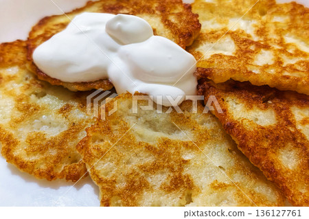 Crispy potato pancakes sit on a plate topped with a dollop of sour cream. This dish is enjoyed during a meal at home with family or friends Crispy potato pancakes sit on a plate topped with a dollop of sour cream. This dish is enjoyed during a meal at home with family or friends 136127761