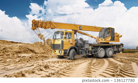 A truck crane is ready for work at a construction site. A large pile of sand is visible in the background, indicating ongoing construction work A truck crane is ready for work at a construction site. A large pile of sand is visible in the background, indicating ongoing construction work 136127780