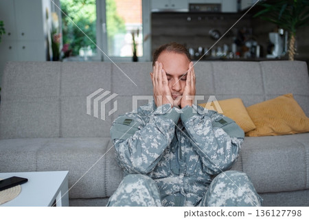 Depressed soldier sitting on the floor at home suffering from post-traumatic stress disorder 136127798