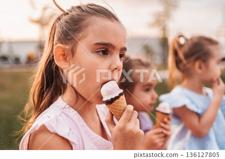 Children enjoying ice cream cones in a park during sunset 136127805