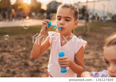 Girl blowing soap bubbles in a park at sunset Girl blowing soap bubbles in a park at sunset 136127809