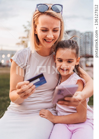 Mother and daughter shopping online using a credit card and a smartphone 136127812
