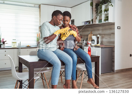Two young women taking a break from cleaning the kitchen and using a smartphone Two young women taking a break from cleaning the kitchen and using a smartphone 136127830