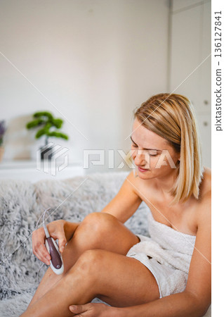 Young Woman Removing Leg Hair with Electric Epilator at Home 136127841