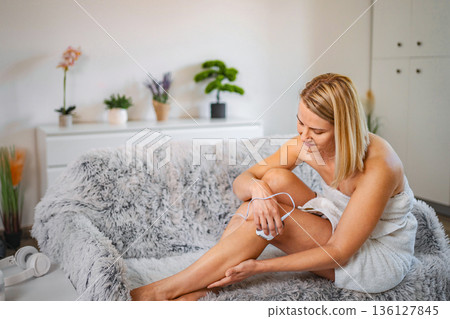 Woman removing leg hair with an electric epilator at home Woman removing leg hair with an electric epilator at home 136127845