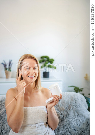 Smiling woman applying face cream at home Smiling woman applying face cream at home 136127850
