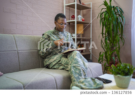 Soldier relaxing at home reading a book and drinking coffee 136127856