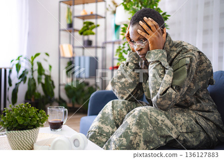 Depressed african american soldier suffering from ptsd sitting on sofa at home Depressed african american soldier suffering from ptsd sitting on sofa at home 136127883