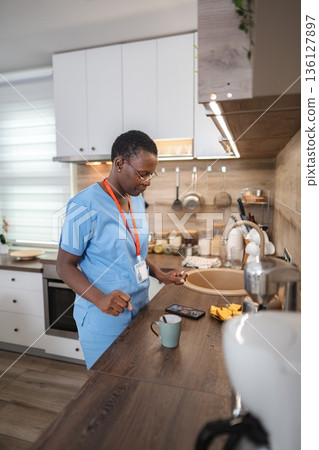 Nurse checking her phone during breakfast in the kitchen Nurse checking her phone during breakfast in the kitchen 136127897