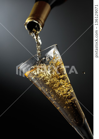 White sparkling wine is poured from a bottle into a glass. 136129071