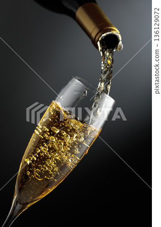 White sparkling wine is poured from a bottle into a glass. White sparkling wine is poured from a bottle into a glass. 136129072