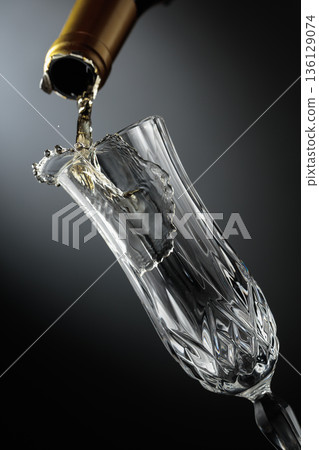 White sparkling wine is poured from a bottle into a glass. White sparkling wine is poured from a bottle into a glass. 136129074