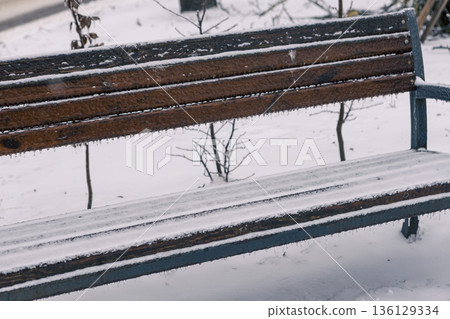 an icy, snow-covered park empty bench with icicles hanging down an icy, snow-covered park empty bench with icicles hanging down 136129334